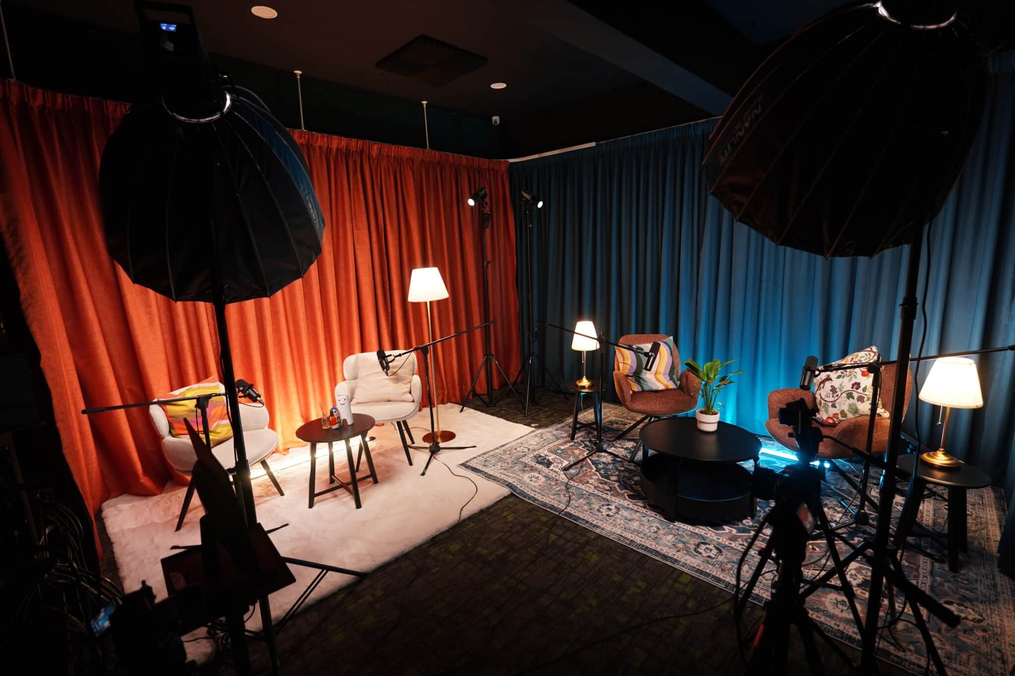 Cozy podcast recording setup with chairs, microphones on stands, and red and blue curtains in the background.